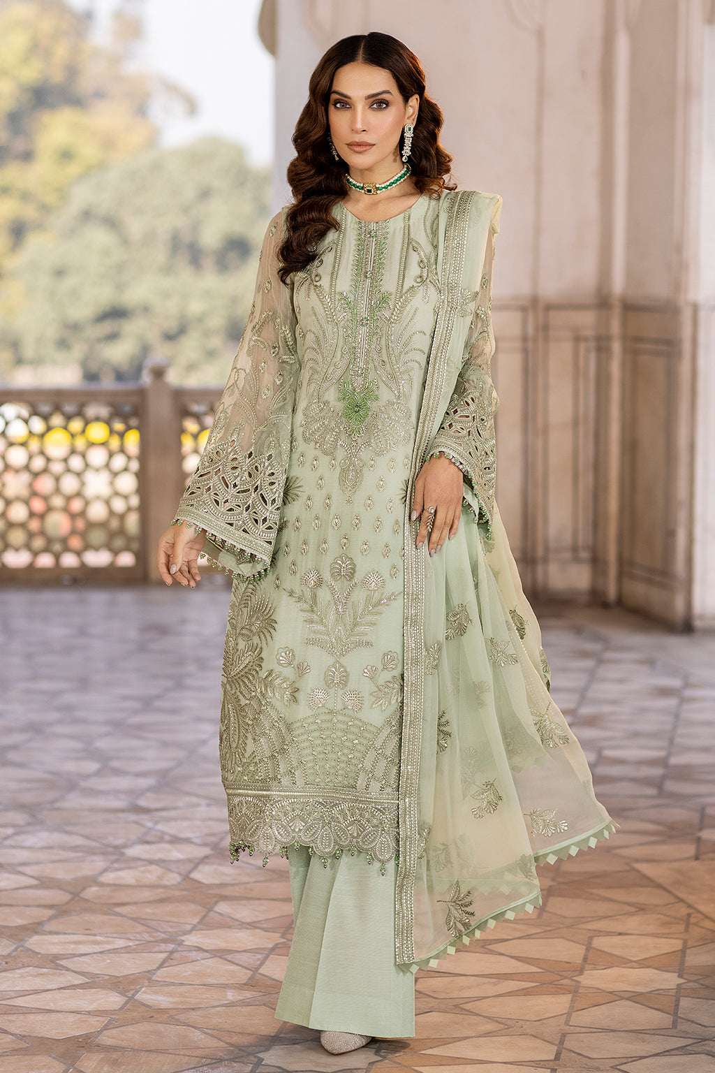 A woman wearing a green embroidered chiffon suit with organza borders and a dupatta.